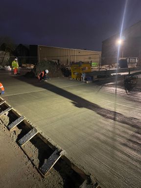 Concrete gang finishing a freshly poured slab under floodlight at night