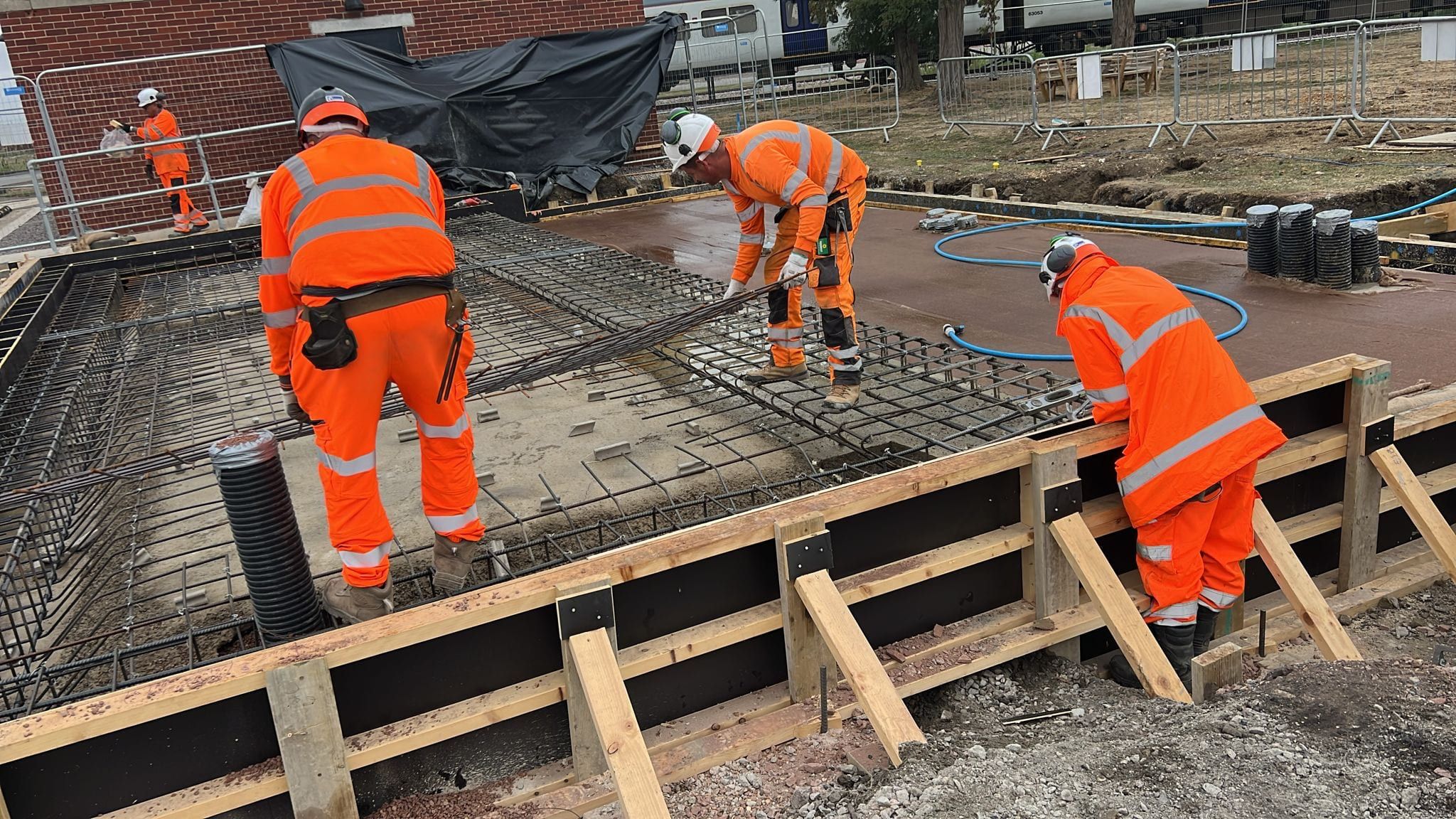 Four workers in helmets and high visibility clothing fixing reinforcement at a shuttered slab edge