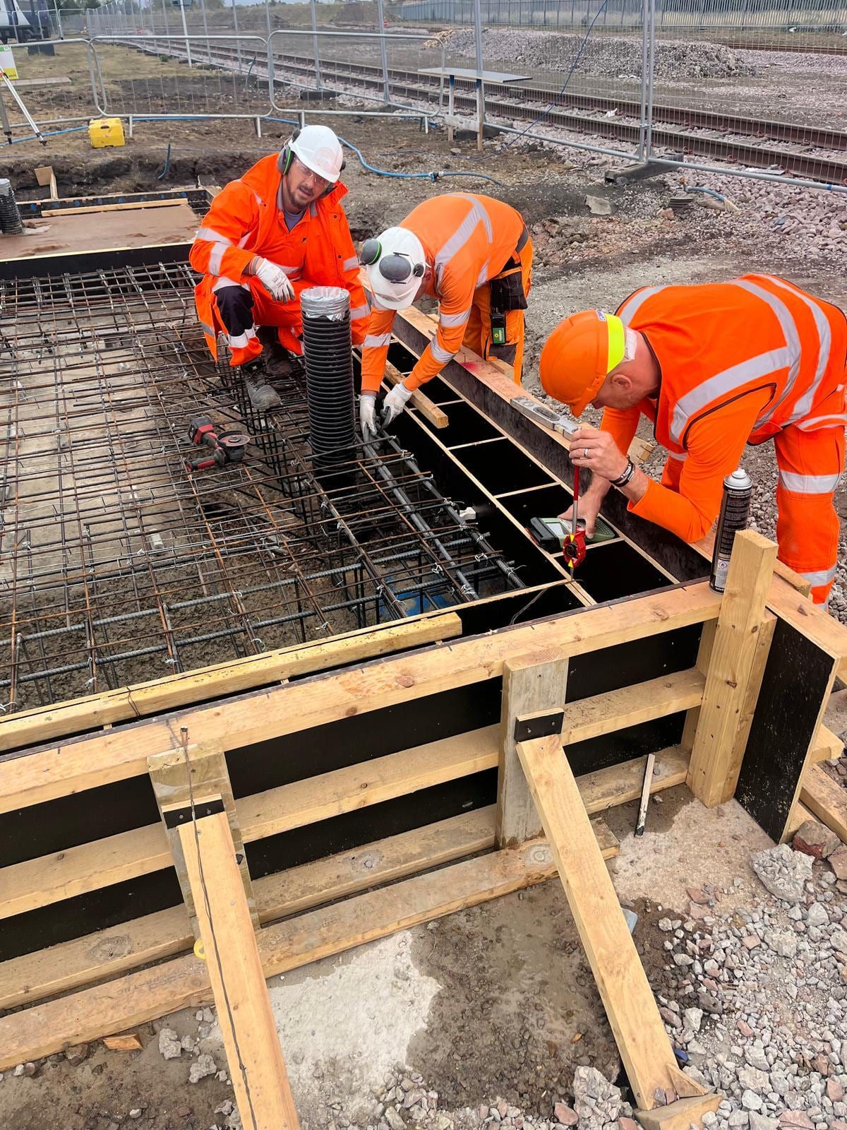 Three workers checking the level of a timber shutter beside a steel reinforcement mat